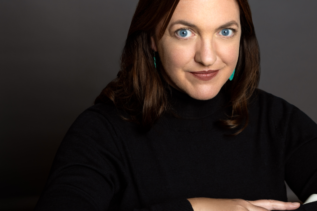 white female with brown hair, blue eyes, black turtleneck, aqua earrings